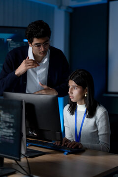 Adult male technology consultant discusses software system with female analyst at computer, supporting cybersecurity review, digital strategy planning, data analysis, and office collaboration.