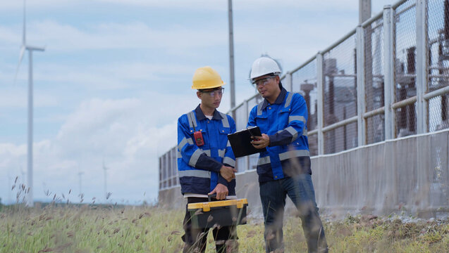 Wind power technicians review a maintenance plan beside renewable energy infrastructure, showing equipment service, engineering teamwork, field diagnostics, safety, and sustainable operations.
