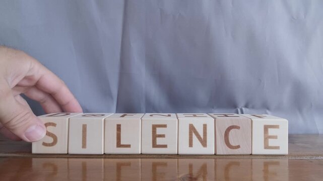motivational word Silence, laying out by hand from letters on wooden cubes, slow motion
