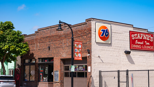 Downtown Eau Claire, WI - Sep 3, 2026: Exterior of The 410 Bar brick building featuring vintage Stafne&rsquo;s Sunset Inn Dining Lounge and 76 gas station sign under a blue sky.