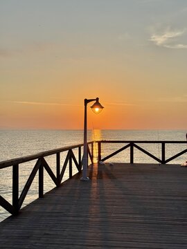 View of sunrise over the sea from a wooden pier with a lamp post in the foreground in Paralia, Katerini, Greece.