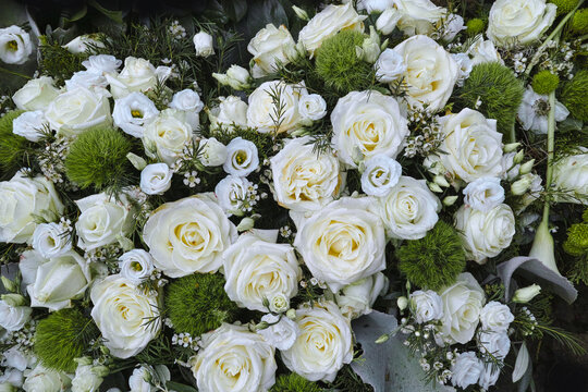 Zur Trauer am Grab liegen die Besten und Sch&ouml;nsten wei&szlig;en Blumen, ein Rosengesteck als Kranz in Draufsicht