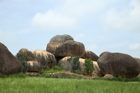 View of the Riyom Rock Formation featuring large, rounded granite boulders set amidst lush green fields and scattered vegetation in Riyom, Plateau, Nigeria.