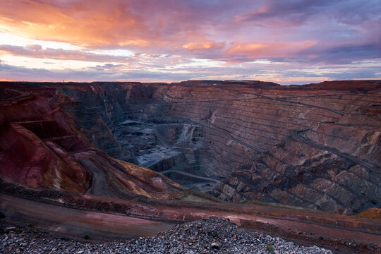 View of the Super Pit open-cut gold mine at sunset with dramatic clouds and terraced rock walls in Kalgoorlie-Boulder, Western Australia, Australia.
