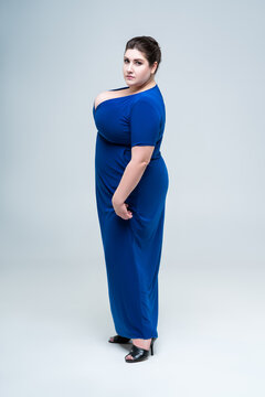 Plus size fashion model in blue long dress with deep neckline, fat woman on gray background, body positive concept