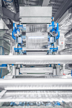 View of industrial machinery processing metallic foil with rollers and precision components in a factory setting in Berlin, Berlin, Germany.