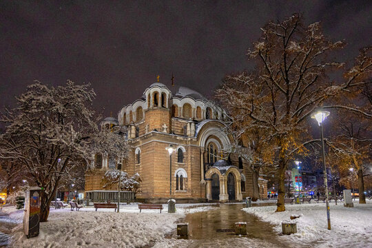 View of Saint Nedelya Church illuminated at night during a winter snowfall with snow-covered trees and benches in the surrounding park in Sofia, Sofia City Province, Bulgaria.