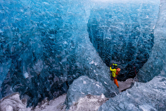 View of a hiker in bright gear exploring the deep blue ice formations inside a glacier cave at Jokulsarlon, Sveitarfelagid Hornaf, Iceland.