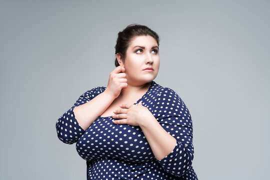 Portrait plus size fashion model in blue polka dot dress, fat woman on gray background, body positive concept