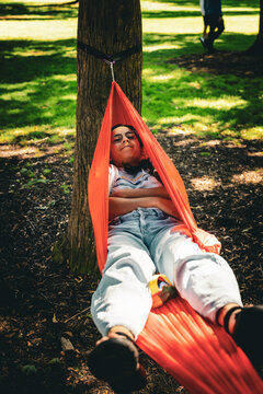 Woman resting with folded arms in a hammock beneath a tree