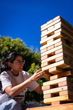 Woman reaching toward a tall wooden block tower outdoors