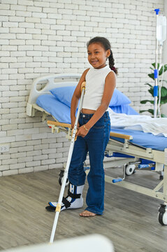 A young girl smiling confidently while using a crutch in a bright hospital room. She embodies resilience and positivity in challenging times.