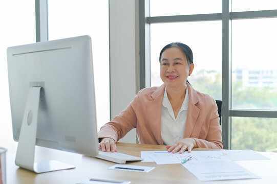 Happy businesswoman working in a modern office, engaged in her tasks. She smiles while using a computer and surrounded by documents.