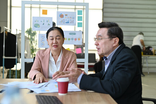 Two business professionals discussing strategies over paperwork in a modern office environment, showcasing teamwork and collaboration.