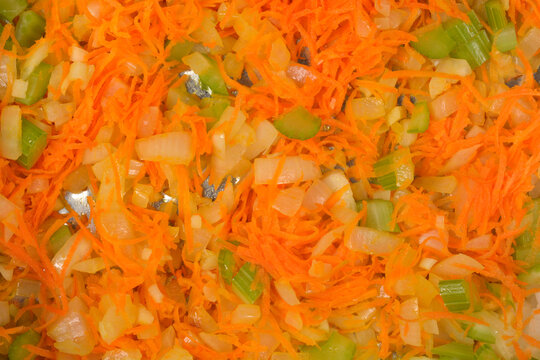 A close up top view shot of a traditional mirepoix mixture with grated carrots diced onions and celery sauteing in a pan.