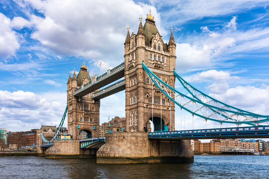 View of the iconic Tower Bridge with its blue suspension cables and stone towers rising above the River Thames under a bright blue sky in London, England, United Kingdom.