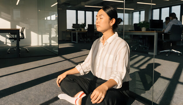 A young woman sits in a meditative pose on the floor of a professional office with practice mindfulness relaxation relaxation during workday