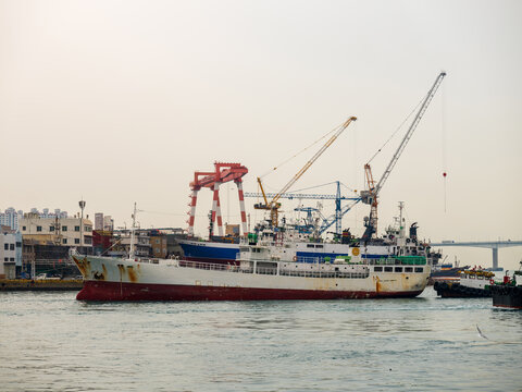 View of a cargo ship docked in the industrial harbor with large cranes and port infrastructure in the background in Busan, Busan, South Korea.