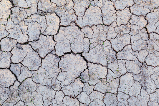 Dry cracked earth forms a dense mosaic of polygon shaped clay segments across an arid landscape shaped by prolonged drought. Seen from an overhead angle, the parched surface reveals deep fissures, fra