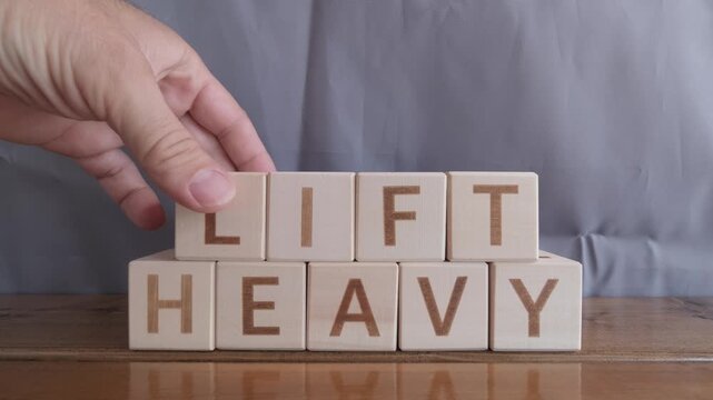motivational word Lift heavy, laying out by hand from letters on wooden cubes, slow motion

