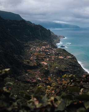 View of Arco de Sao Jorge nestled along dramatic cliffs with lush hills, winding roads, and the Atlantic Ocean in Arco de Sao Jorge, Madeira, Portugal.