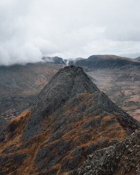 View of the rugged rocky peak of Tryfan mountain surrounded by dramatic hills and a cloudy sky in Bangor, Wales, United Kingdom.