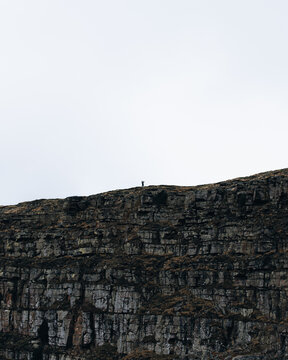 View of a lone hiker standing on the edge of the limestone cliff at Malham Cove in Malham, England, United Kingdom.