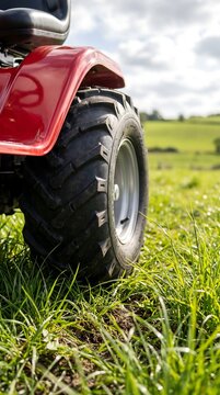 Red ATV Quad Bike Rear Wheel with Knobby Tire on Green Grass in Rural Field: Off-Road Vehicle, Agriculture, Farm, and Countryside Concept