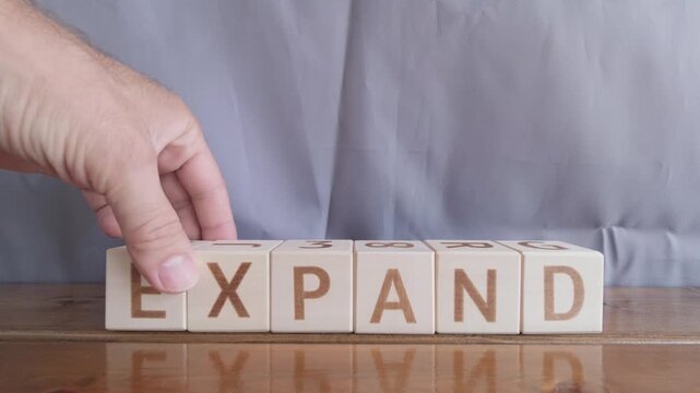 motivational word Expand, laying out by hand from letters on wooden cubes, slow motion
