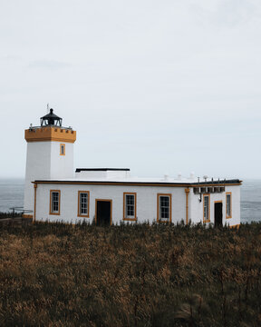 View of Duncansby Head Lighthouse with its white walls and yellow trim, set against a cloudy sky and the North Sea in Wick, Scotland, United Kingdom.