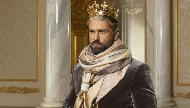 A man wearing a crown and luxurious clothing in an ornate room.