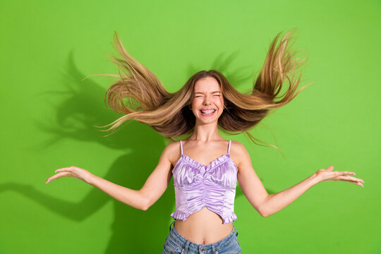 Glamorous young woman with long blonde hair jumping with joy against a vivid green background in a casual stylish lifestyle shot for fashion advertising