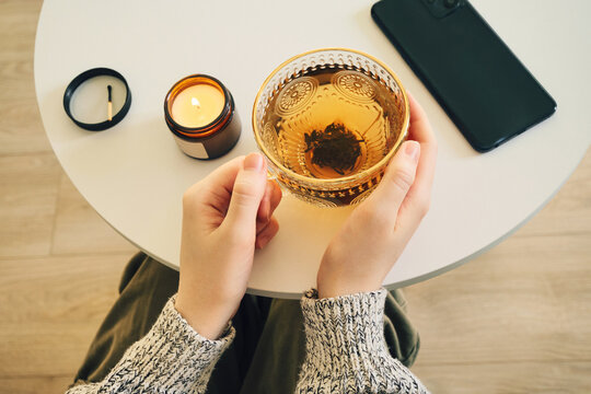 Woman practicing digital detox with smartphone set aside, enjoying tea and candle at home