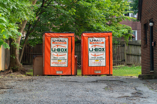 Two bright orange U-Haul U-Box moving containers parked on a gravel driveway, ready for residential or commercial relocation and storage services, surrounded by green trees and a fence.