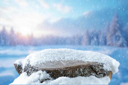Empty covered with snow tree trunk for product placement, surrounded by fresh snow and a beautiful winter landscape in the background.