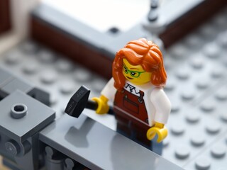 Fototapeta premium Tambov, Russian Federation - June 24, 2026 A close-up shot of a Lego minifigure woman with red hair holding a hammer while working on a grey structure