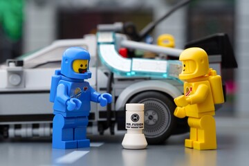 Fototapeta premium Tambov, Russian Federation - September 17, 2026 Blue and yellow Lego spaceman minifigures standing next to a Mr. Fusion generator with a DeLorean time machine in the background.