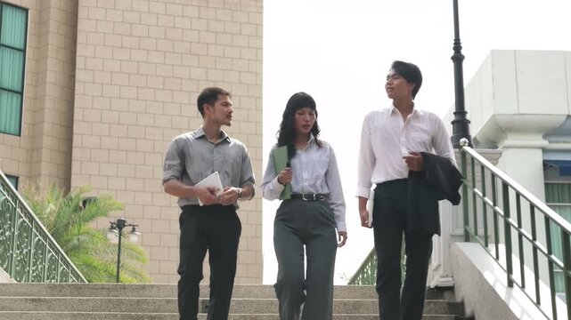 Three young Asian business colleagues discussing a project while looking at a green document folder outdoors in front of a building.