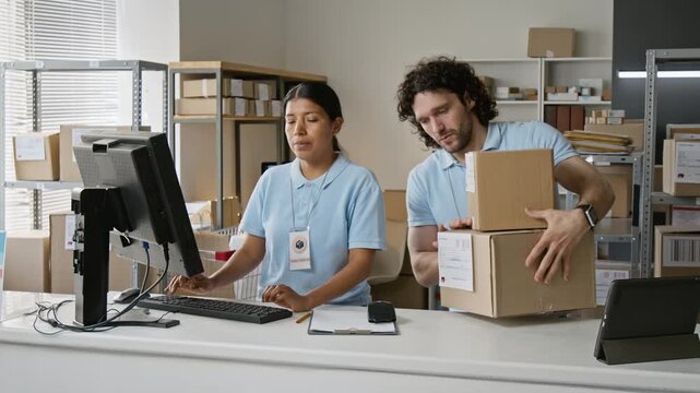 Young Hispanic woman and Caucasian man scanning cardboard parcels with barcode reader and using computer at delivery office. Perfect for logistics service and supply chain video ads