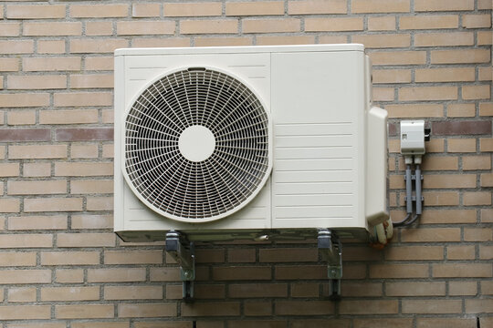 Airconditioning unit installed on brick wall. Summer heat wave prevention electronic cooling and ventilation appliance.