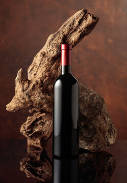 Bottle of red wine with old wooden snag and a piece of granite rock on a broen background.