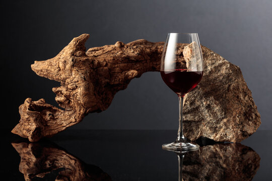 Glass of red wine with old driftwood and a piece of granite rock on a black reflective background.