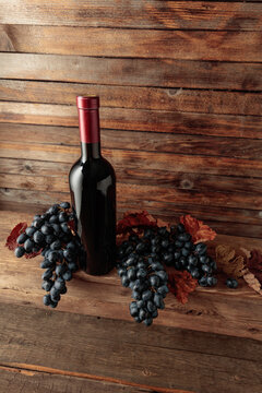Red wine bottle with blue grapes on an old wooden table.