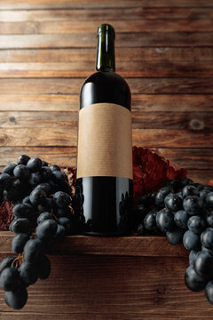Red wine bottle with blue grapes on an old wooden table.