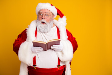 Obraz premium Santa Claus reading a book with a surprised expression against a bright yellow background, festive holiday portrait in classic red suit and white beard