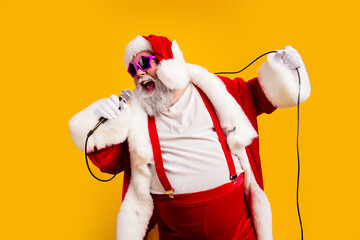 Obraz premium Santa Claus singing into a microphone with pink sunglasses and festive costume on a bright yellow background