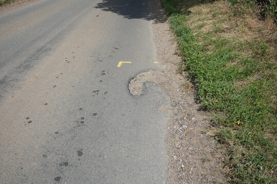 Pothole with yellow paint marking on a damaged rural road surface