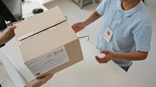 Unrecognizable young worker handing cardboard parcel package to customer over service desk, top view. Footage suitable for e-commerce delivery logistics and postal shipping services