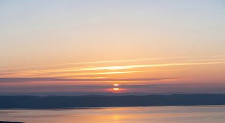 Fototapeta premium A breathtaking golden hour landscape features the sun gently setting over a calm ocean horizon while vibrant orange and pink hues illuminate the dusky evening atmosphere creating a peaceful mood