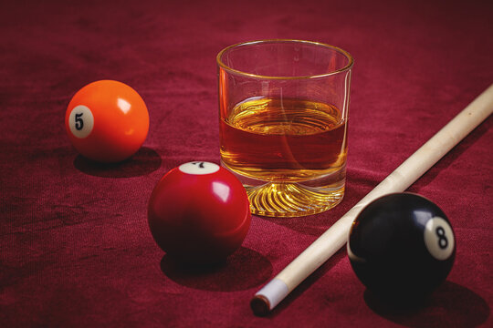 Glass of whiskey with billiard balls and cue stick on a dark table
